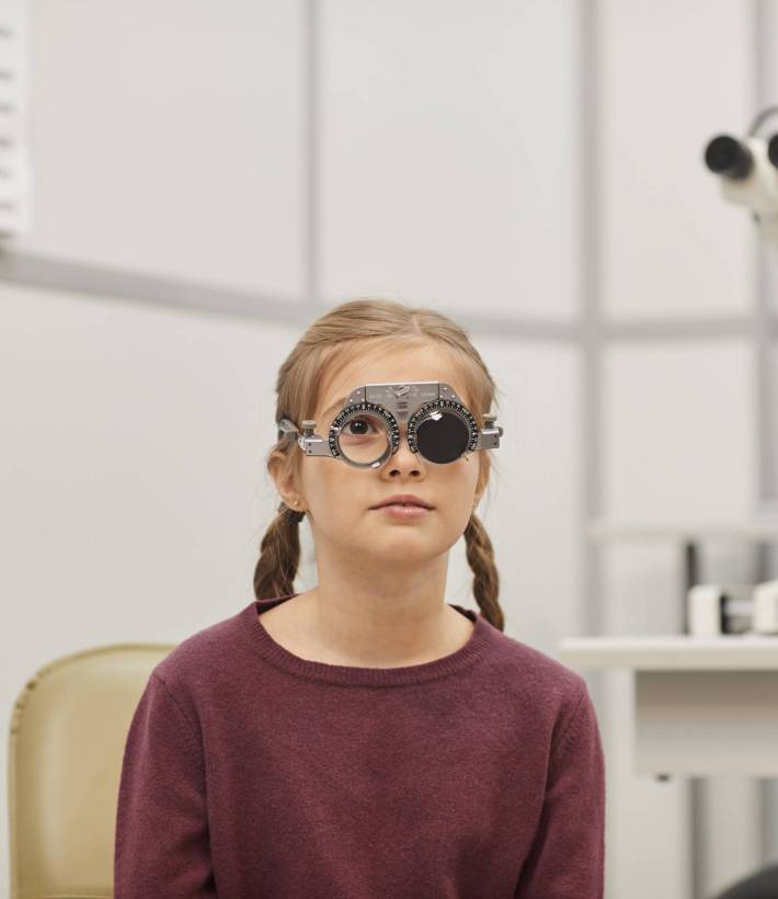 Portrait of cute little girl wearing trial frame during vision test in pediatric ophthalmology clinic, copy space